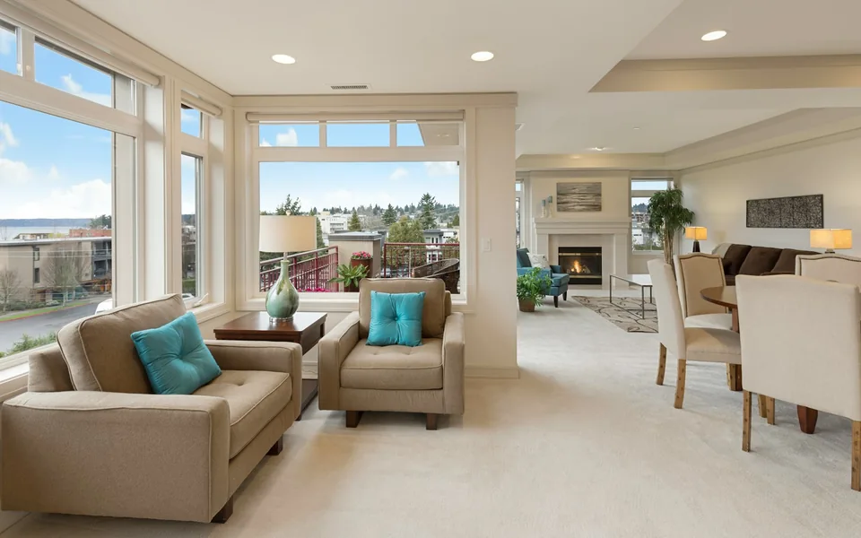 Bright living room with upholstered chairs, large windows and a fireplace.